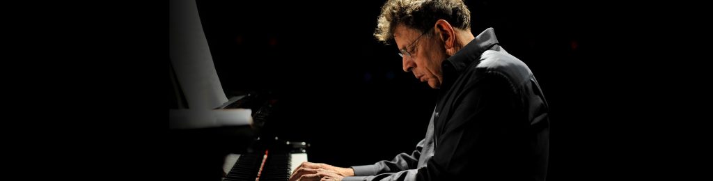 Philip Glass, composer, sits at a piano.