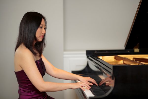 A woman in a dress plays the grand piano.