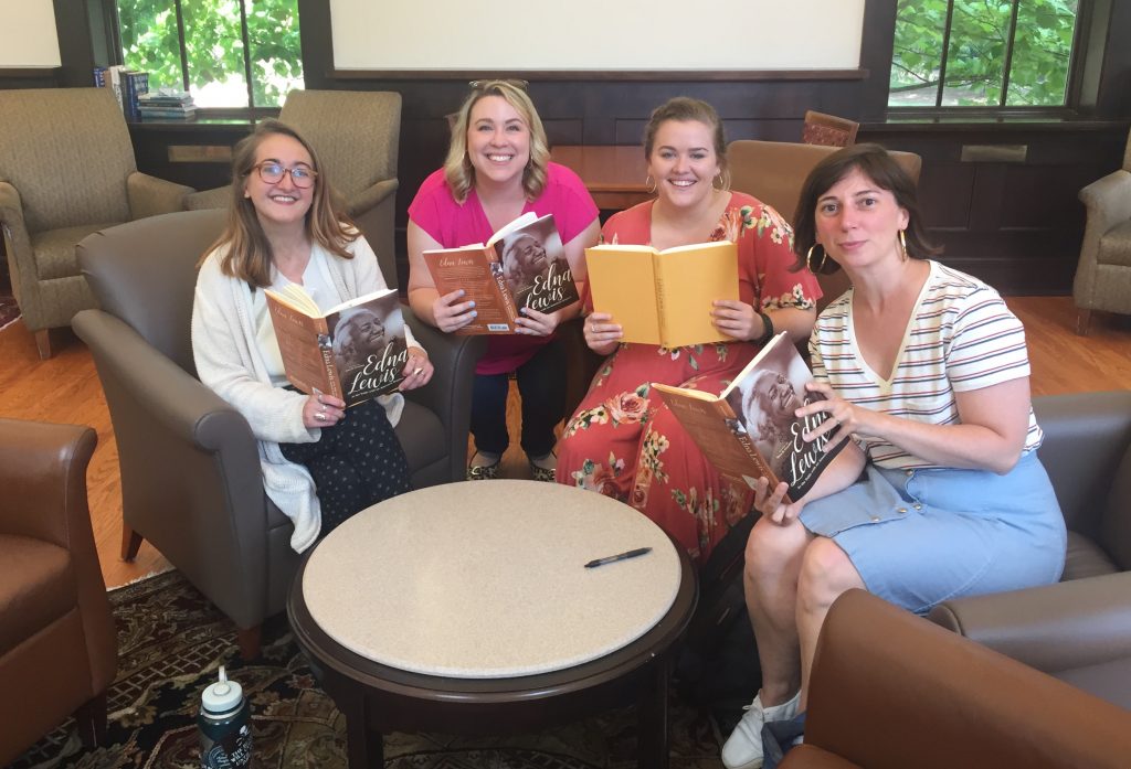 Four women smile as they hold books they've been reading and discussing together.
