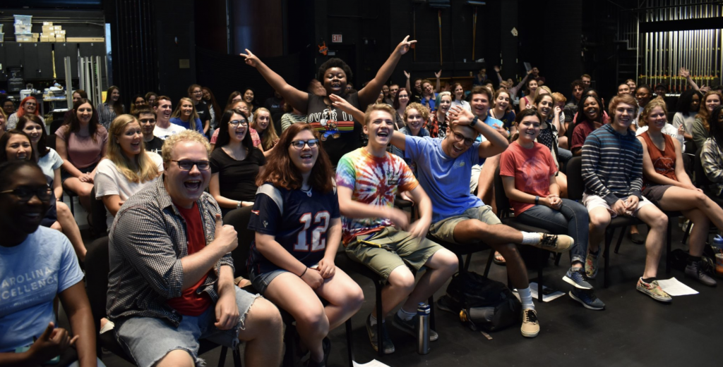 Students smile and cheer at the beginning of student staff orientation on Memorial Hall's stage.