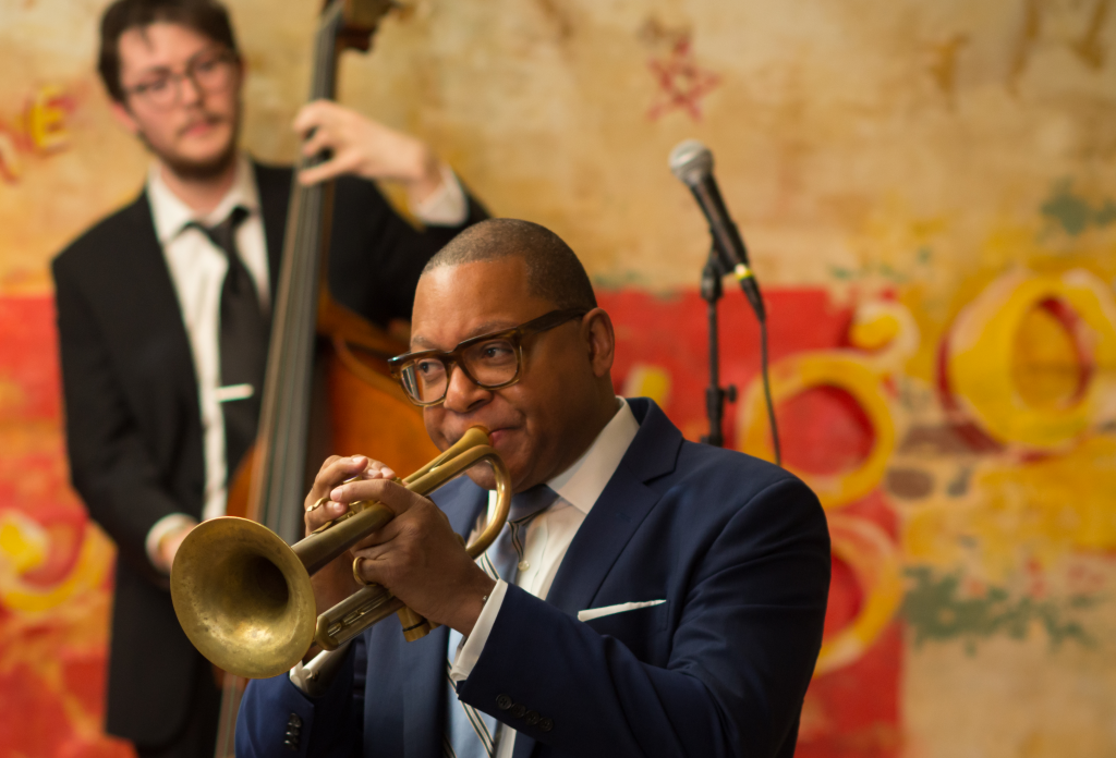Musician Wynton Marsalis plays the trumpet in front of a colorful mural.