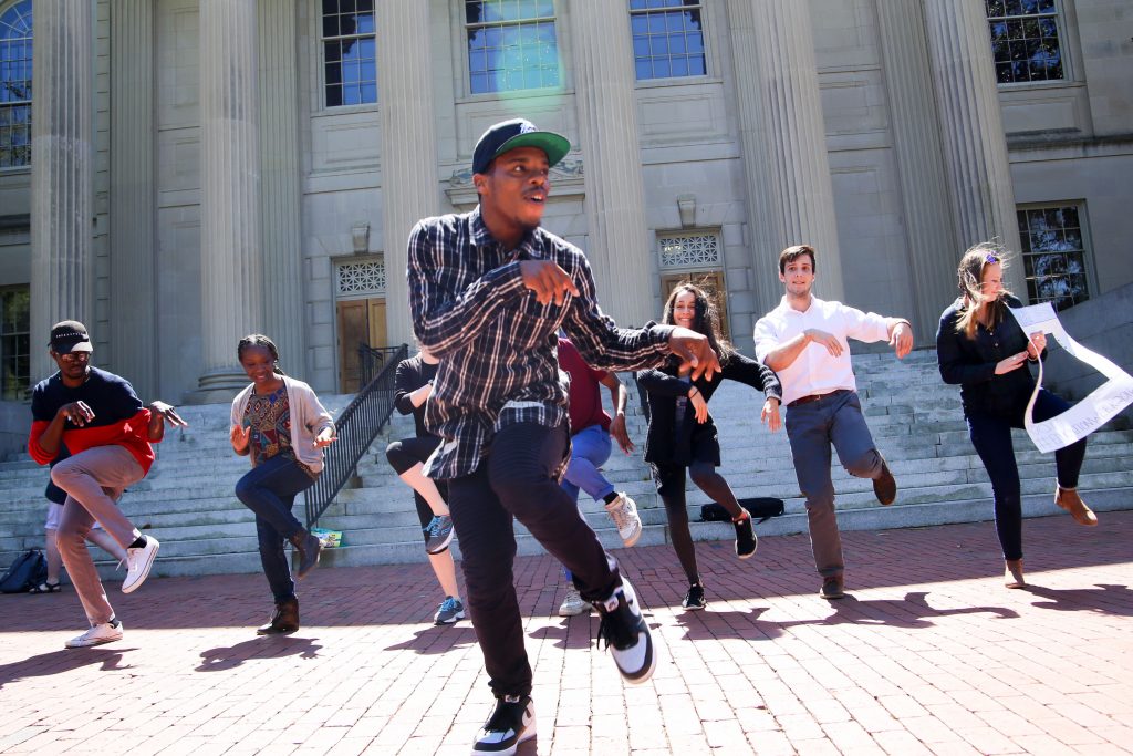 Young man (dancer Lil Buck) dances with seven students lined up behind him outside Wilson Library at the University of North Carolina at Chapel Hill as part of the Carolina Performing Arts' pop-up event