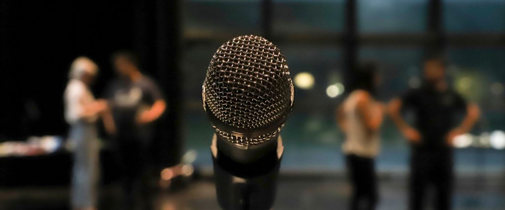 close up image of a microphone on a stand with blurred people standing in the background