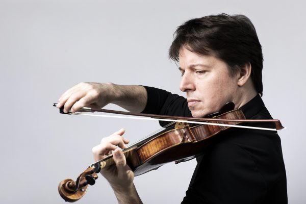 Violinist Joshua Bell holds a violin under his chin, playing the instrument with a pensive look on his face.