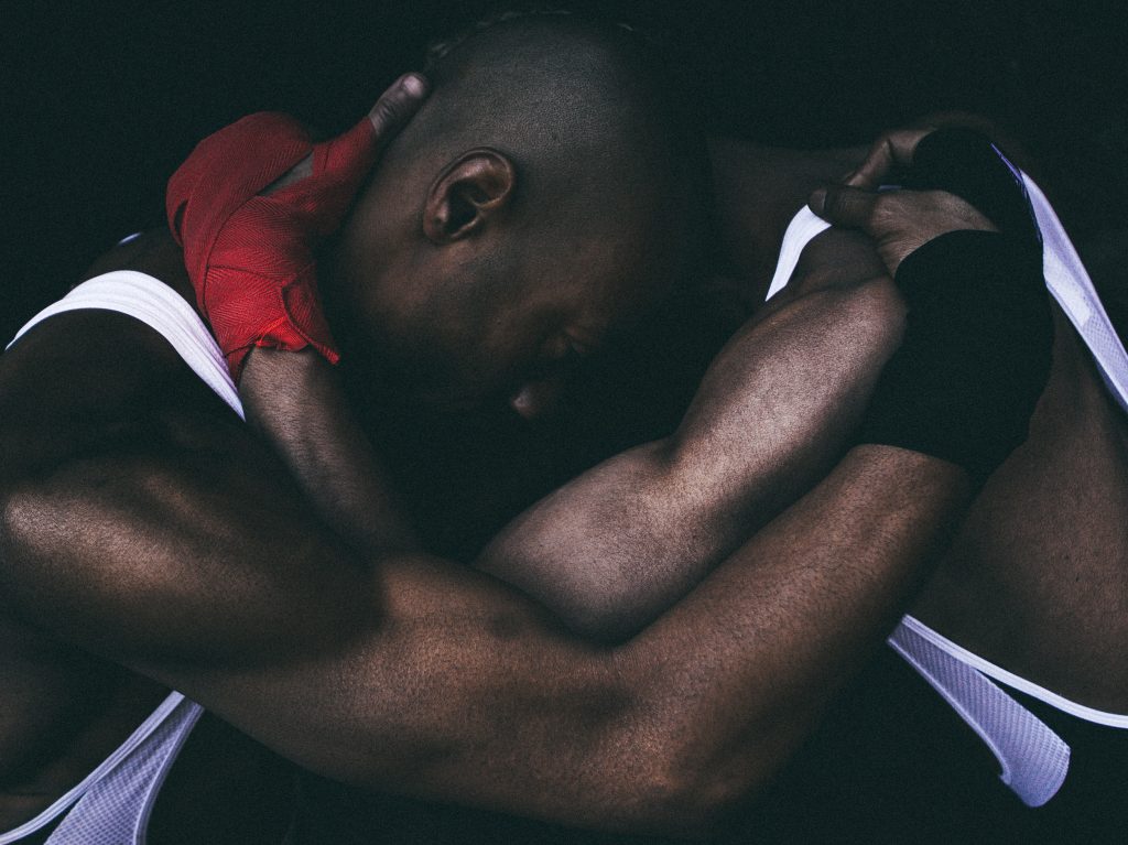 two Black men in white sleeveless shirts locked in embrace at the neck