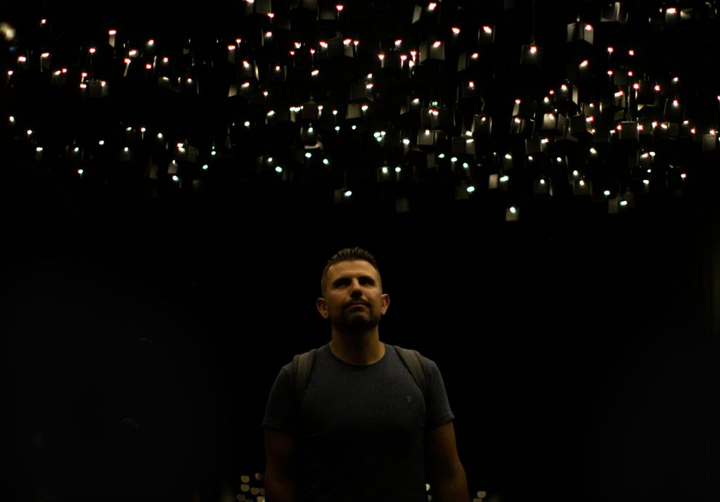 A man stands beneath hundreds of teardrop-shaped lights and speakers at Atmospheric Memory.