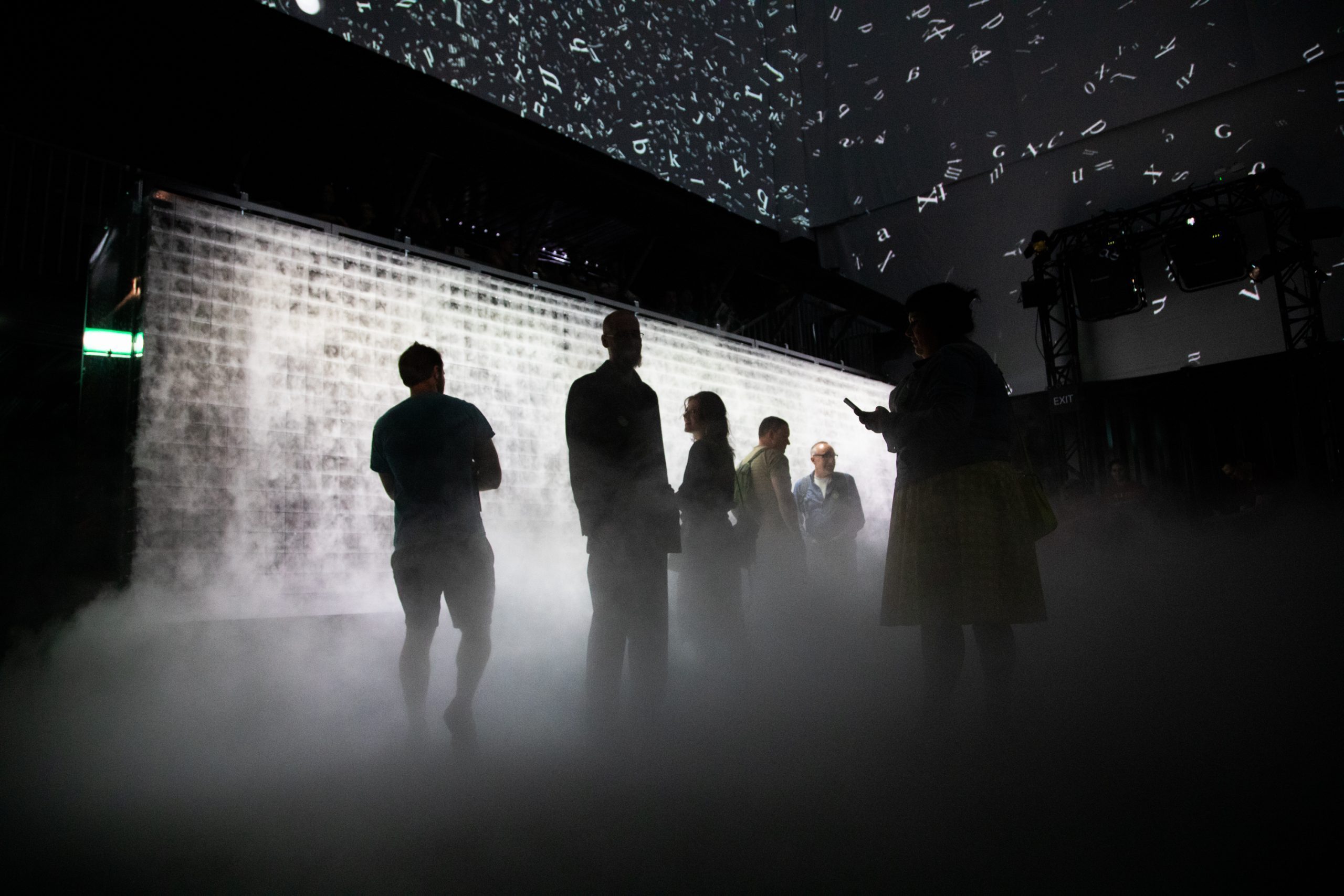 People stand in front of a large wall of smoke inside the Atmospheric Memory installation.