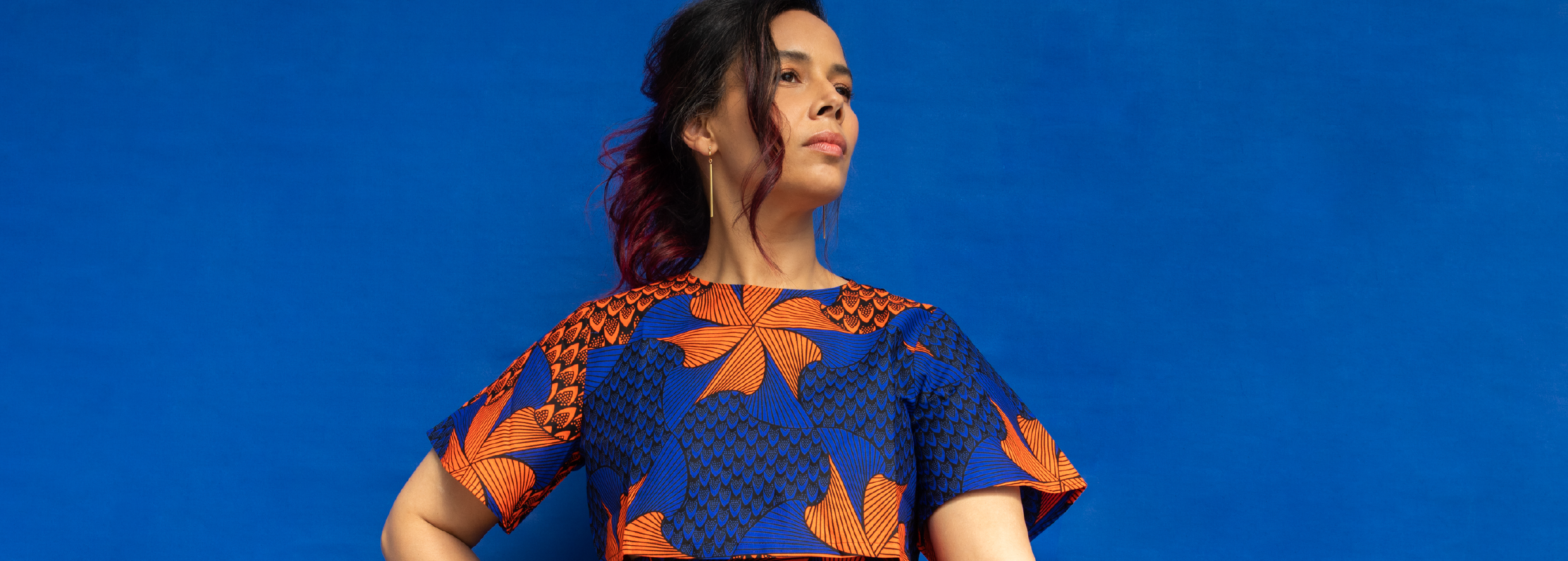 Rhiannon Giddens stands looking over her left shoulder wearing a colorful blue and orange dress.