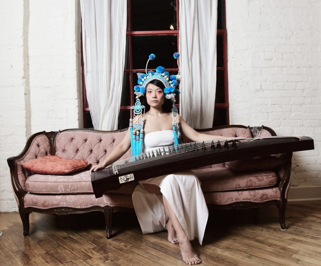 Woman sits on a sofa, holding a guzheng.