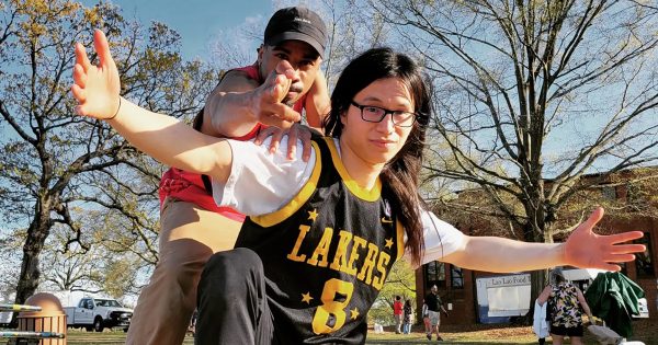 Two break dancers from The Raleigh Rockers pose outside, against a background of trees. One is wearing a Lakers jersey.