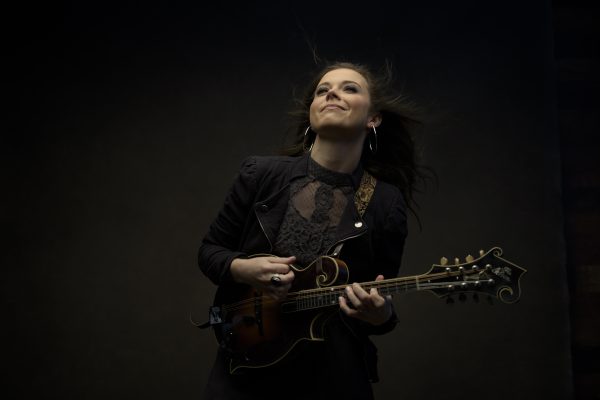 A woman plays mandolin against a black background.